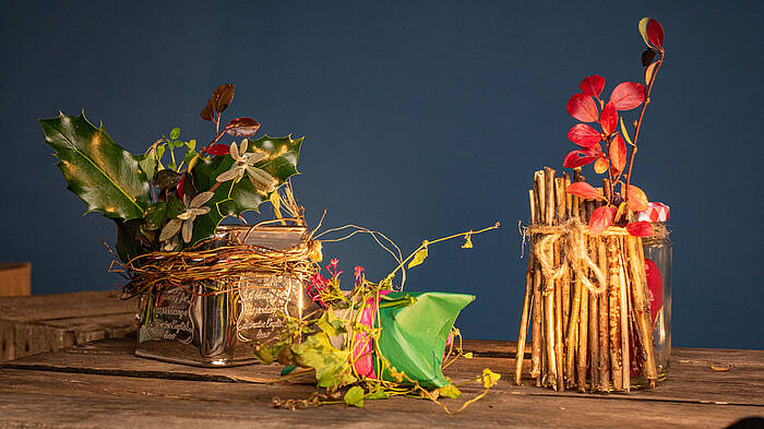 Eine alte Teedose, eine bemalte und gefaltete Klopapierrolle und ein mit Zweigen verziertes Glas stehen nebeneinander